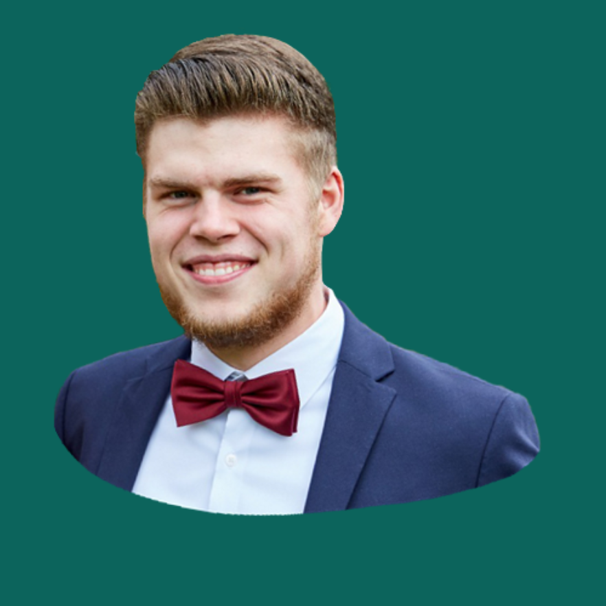Junger Mann mit blondem Haar, Bart und roter Fliege, lächelt in einem Anzug.